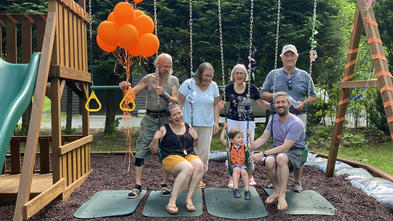 Wish kid Jasper sitting on a swing o his swingset with his family surrounding