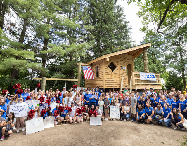 A crowd of Make-A-Wish supporters gathered around wish kid Kyle in front of his new treehouse